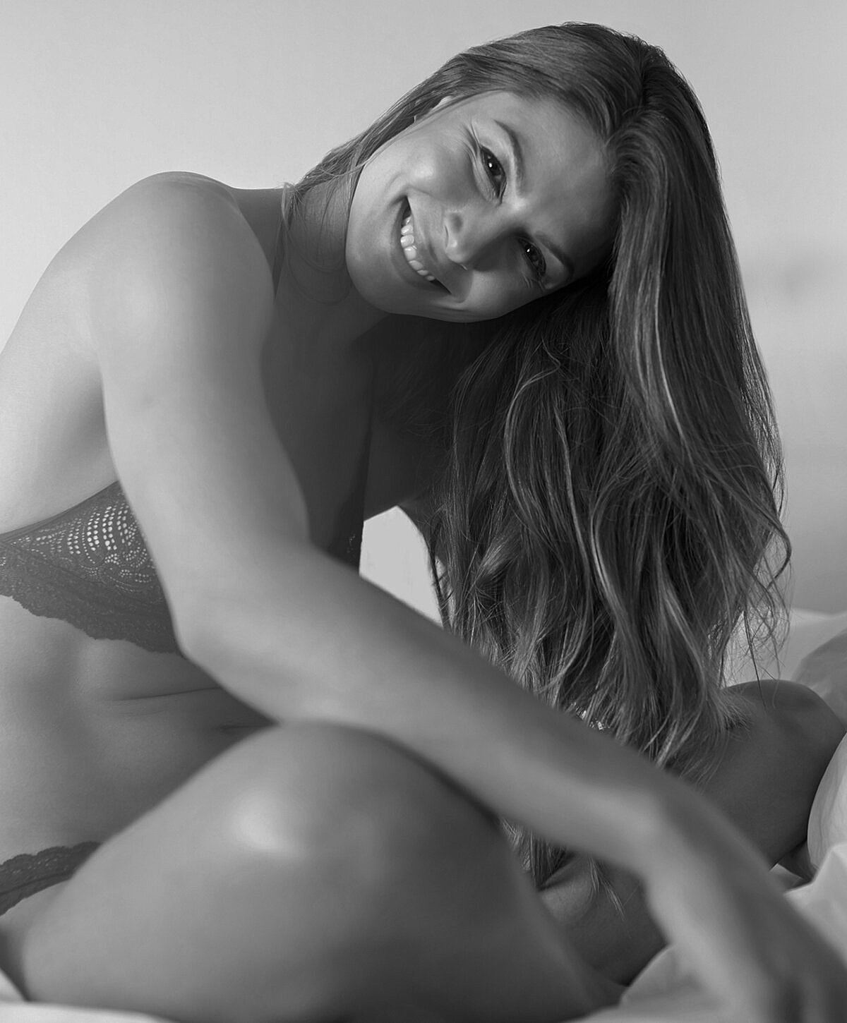 Smiling woman in lingerie sitting on bed.