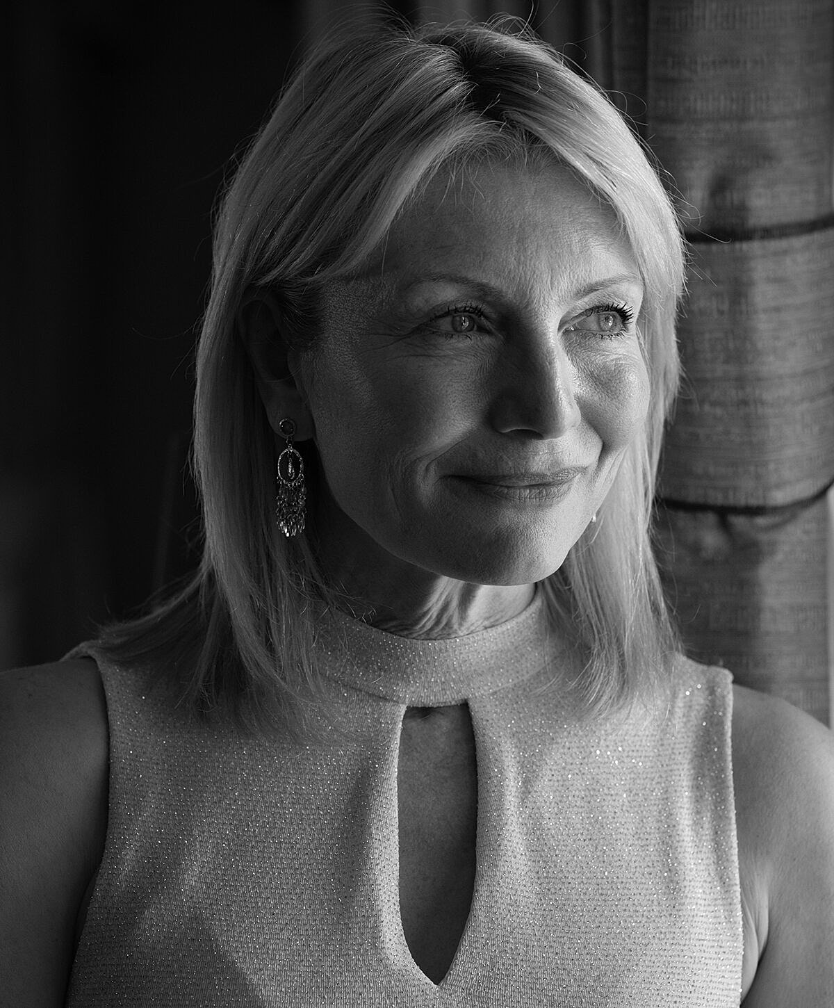 Woman smiling near window in black and white.