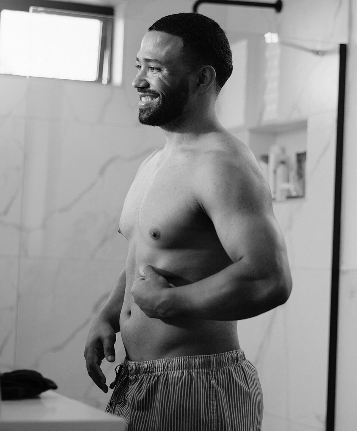 Man smiling in bathroom, wearing striped shorts.